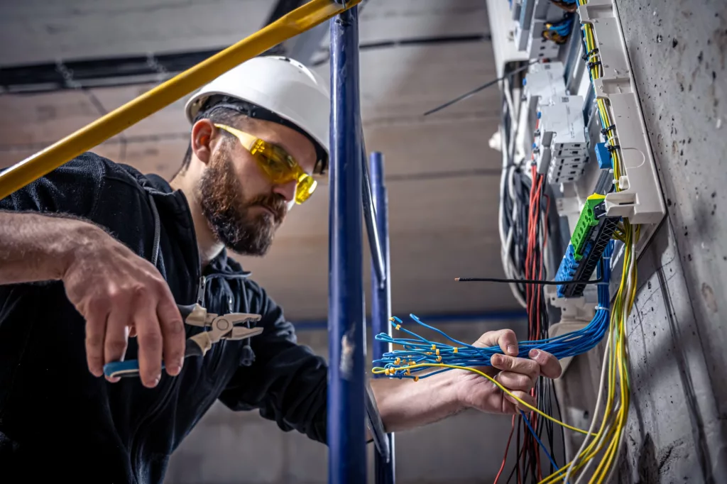 A male electrician works in a switchboard with an electrical connecting cable.